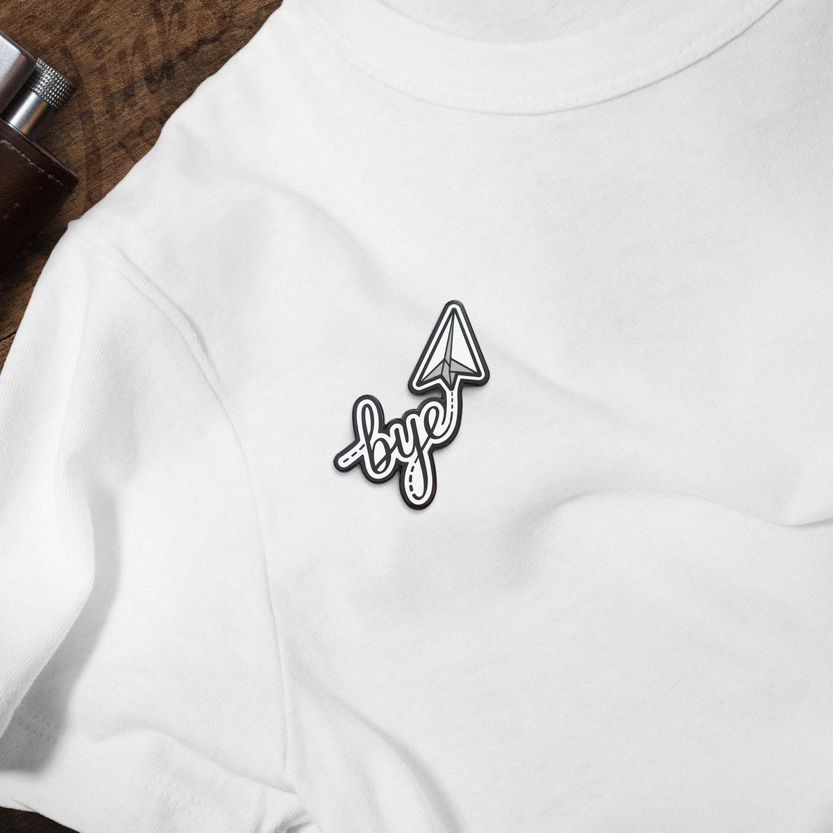 Bye Paper Airplane hard enamel pin on white t-shirt