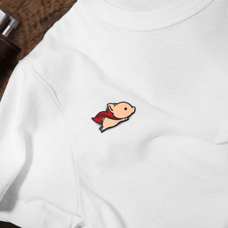 Flying Pig with Red Superhero Cape hard enamel pin on white t-shirt